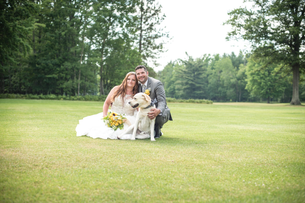 Bride and Groom sitting on the grass with their yellow lab at a golf course in St. Helen, mi, after their wedding.