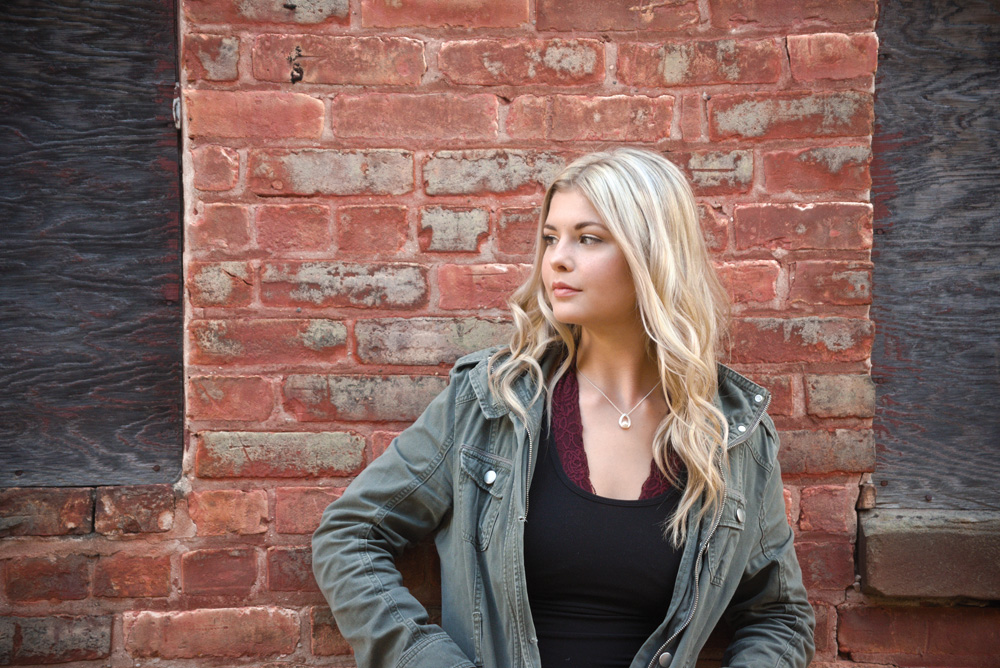HIGH SCHOOL SENIOR GIRL LEANING ON BRICK WALL