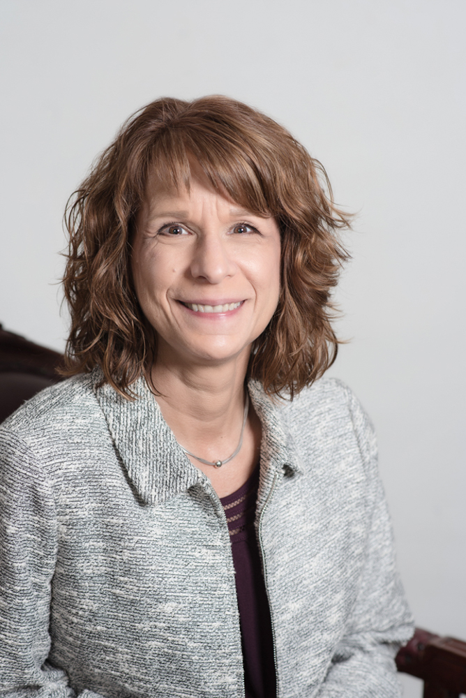 headshot of a woman sitting down on a chair with gray jacket