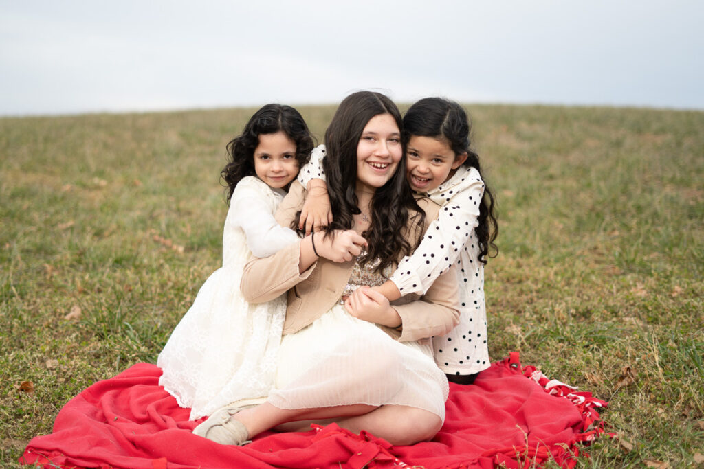 Three girls of different ages hugging on a blanket.