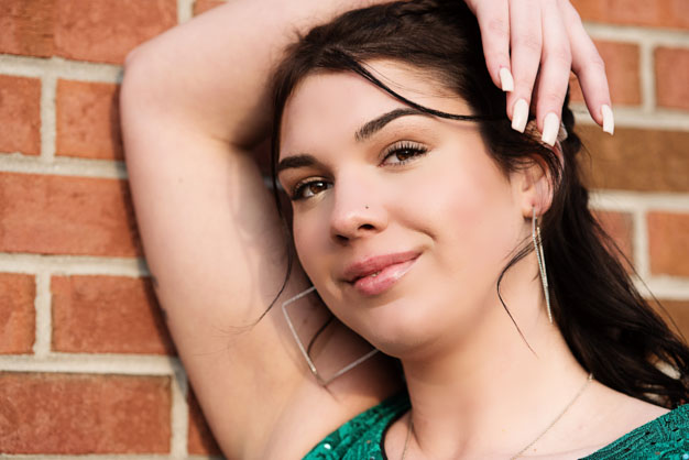 High School senior leaning on brick wall with manicure nails