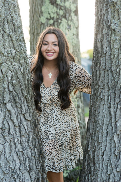 High School Senior standing inbetween three tree trunks