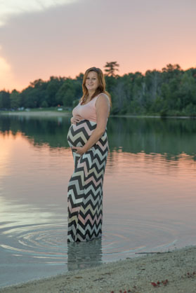 pregnant woman standing in lake at sunset.