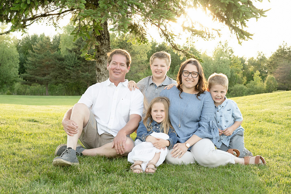 Family of 5 sitting in grass at sunset on Sugar Springs Golf Course in Gladwin