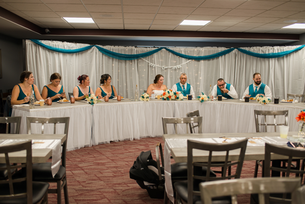 Wedding party sitting at curved table ready to eat dinner at a banquet hall in West Branch.