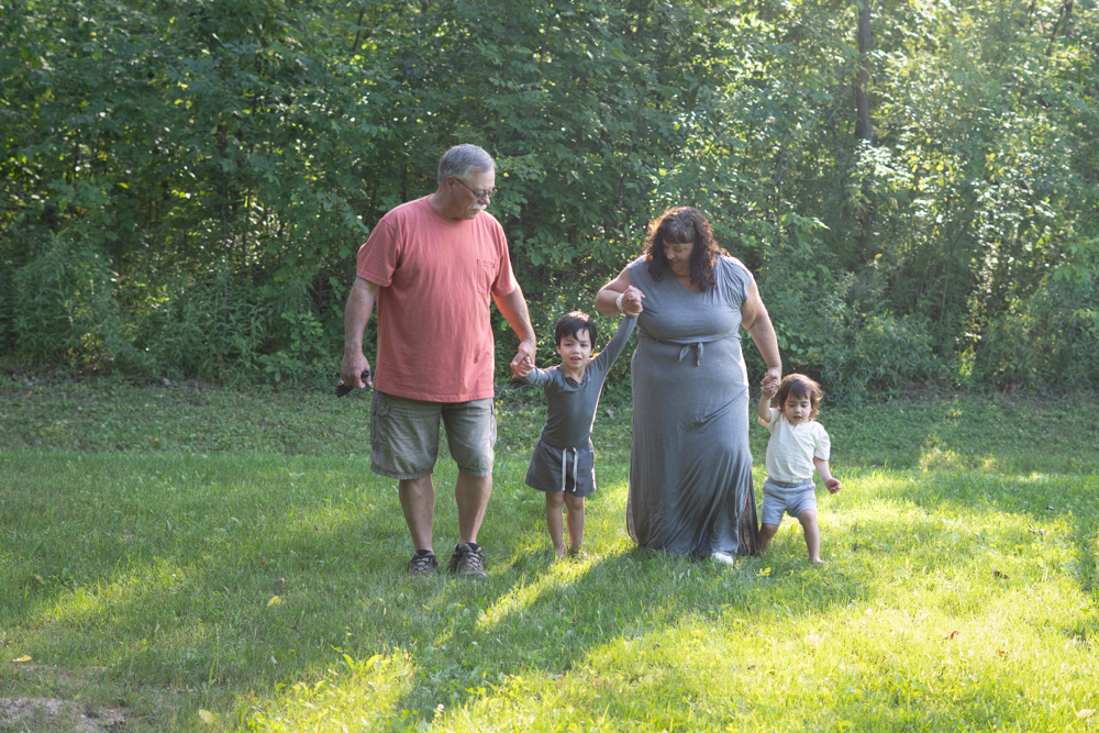 Grandparents walking across the yard holding two grandsons by the hand.