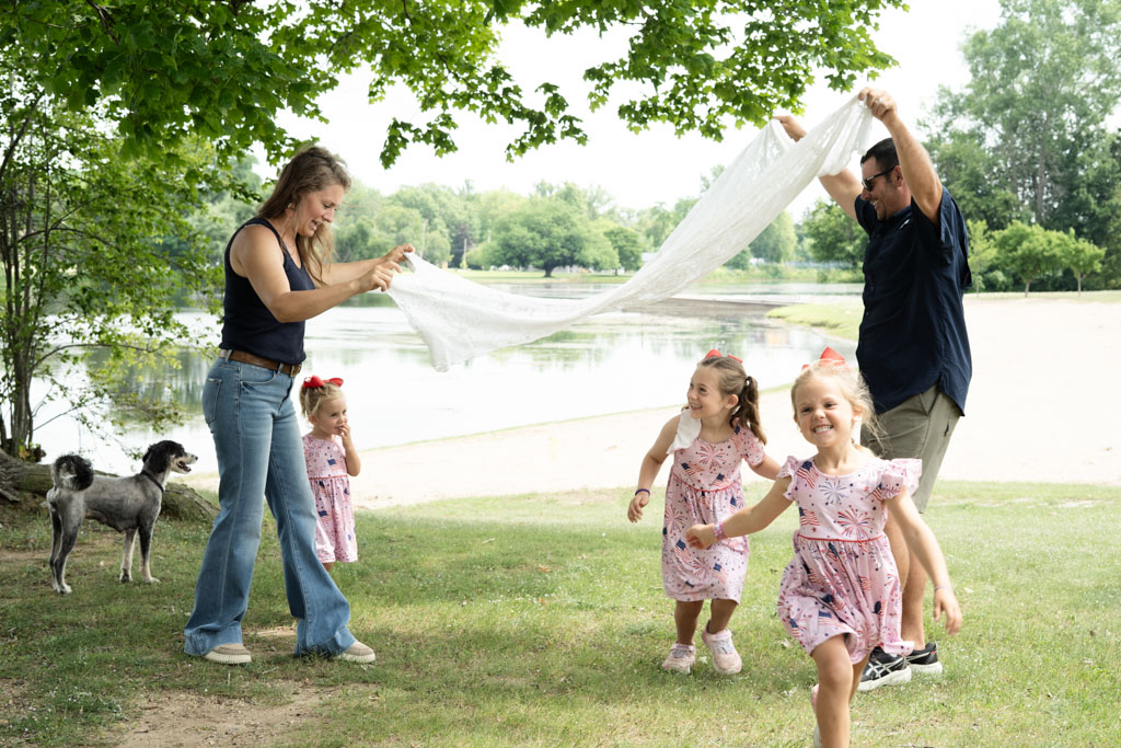 Mom and Dad play London Bridges with their three young girls with the dog standing by.