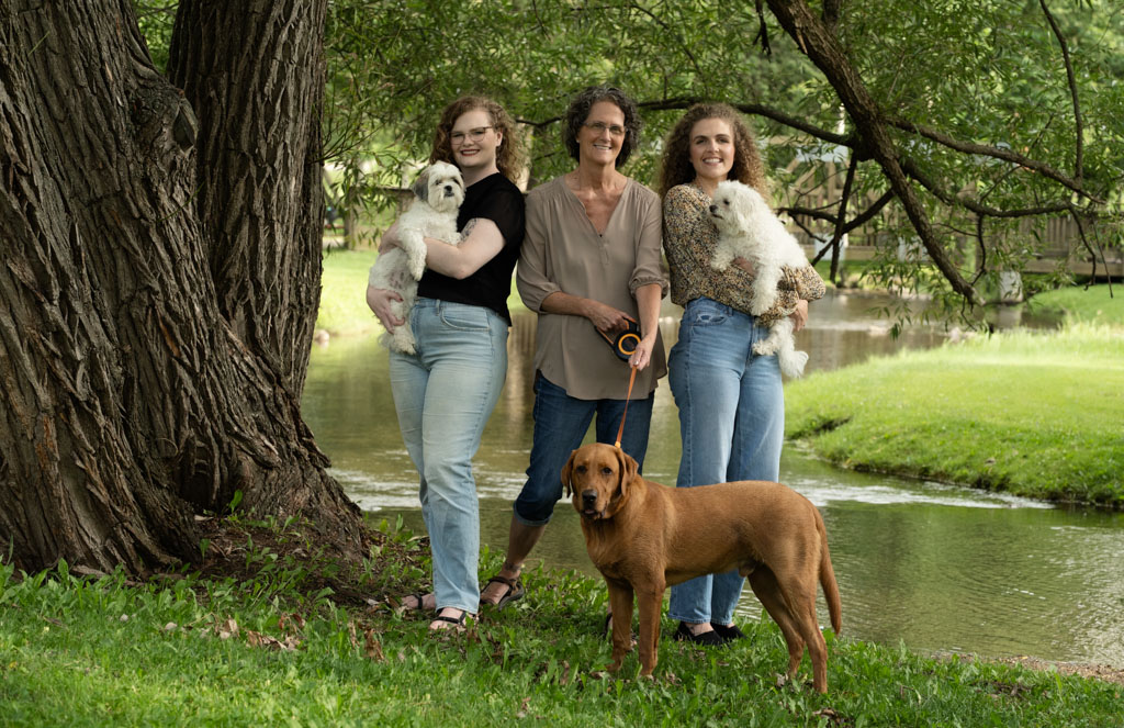Three woman standing by Houghton Creek holding their dogs.